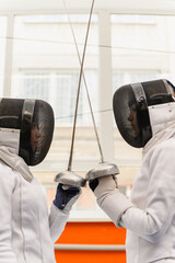 Close-up of female fencers crossing epees before match indoors.