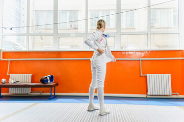 Female fencer putting on protective gear before match indoors.