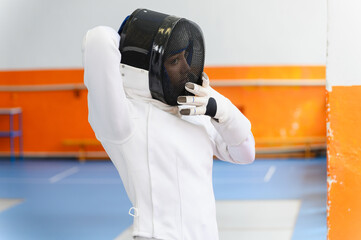 Female fencer adjusting protective mask before match indoors.