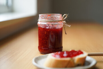 Homemade strawberry jam in a jar with slice of bread on a plate