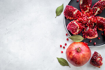 Fresh ripe pomegranate with cut in half and pieces on plate to eat, top view.