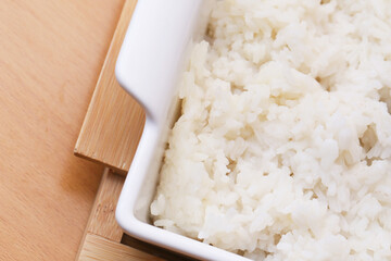 Cooked white rice in ceramic dish. Steamed grains in closeup view. Minimalist food presentation on wooden surface. Healthy meal with simple texture. Asian cuisine with natural ingredients.