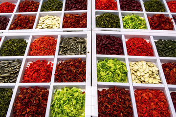 Various colored dried vegetables and seeds in wooden box are sale at market, top view.