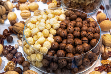 Macadamia nuts in glass bowl among other various nuts in health food store display case. Mixed nuts background.