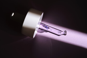 Pipette with serum on purple background with sunlight.