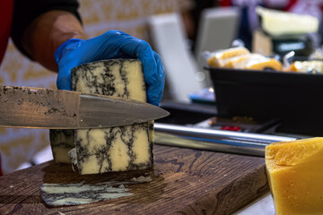 Seller slicing mold cheese on wooden board. Cheese shop.