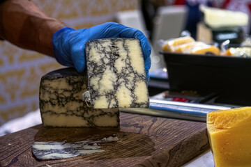 Seller slicing mold cheese on wooden board. Cheese shop.