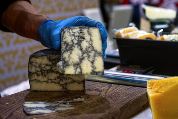 Seller slicing mold cheese on wooden board. Cheese shop.