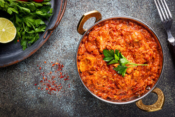 Chicken meat with tikka masala sauce, spicy curry food in iron copper pot with seasonings, top view