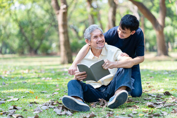 bonding asian family senior father and young adult son enjoy leisure time together in nature,elderly man holding a book and son embracing his father