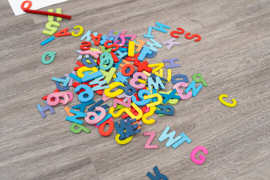 Pile of colorful foam letters and numbers scattered on wooden floor, vibrant educational toy pieces in various shades representing early learning tools for literacy, play-based development and fun