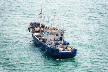 A blue and white fishing boat sails on a calm sea, with gentle waves. The vessel features a deck equipped with fishing gear and a visible wheelhouse. © Mariusz