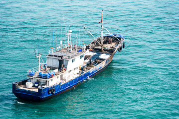 A blue and white fishing boat sails on a calm sea, with gentle waves. The vessel features a deck...
