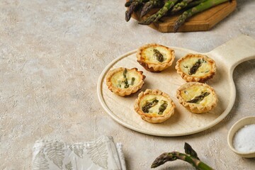 Shortcrust tartlets with asparagus and creamy filling on a ceramic plate on a light concrete background. Recipes asparagus.