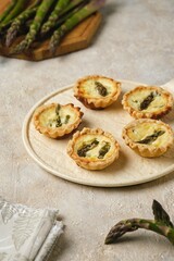 Shortcrust tartlets with asparagus and creamy filling on a ceramic plate on a light concrete background. Recipes asparagus.