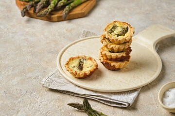 Shortcrust tartlets with asparagus and creamy filling on a ceramic plate on a light concrete background. Recipes asparagus.