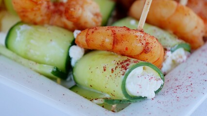 Fresh cucumber shrimp rolls featuring creamy cheese filling, sprinkled with aromatic spices, elegantly plated on crisp white surface