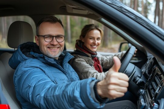 Happy European spouses sitting in new car and gesturing thumbs up, smiling at camera, driving new auto during test drive. Auto leasing concept