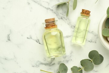 Bottles of essential oil and eucalyptus leaves on white marble table, flat lay