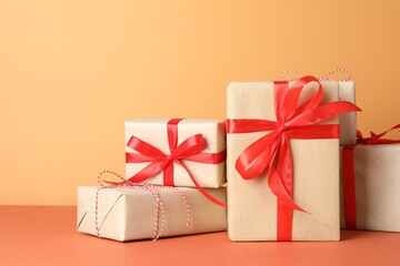 Many gift boxes wrapped in kraft paper on orange table. Space for text