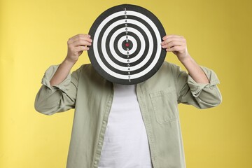 Targeting. Man with dart board on yellow background