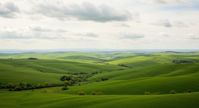 Rolling green hills under a cloudy sky create a peaceful landscape scene.