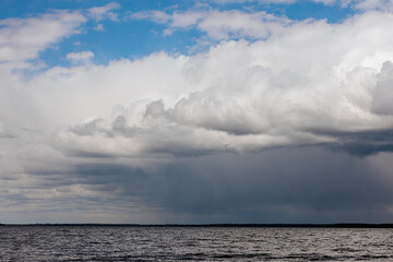 Obraz premium A dark storm approaches over a calm lake, with heavy rain visible on the horizon and dense clouds casting shadows across the sky and water ample copy space.