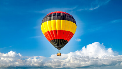 Fototapeta premium Colorful hot air balloon with German colors flag floating high in a clear blue sky on a sunny day