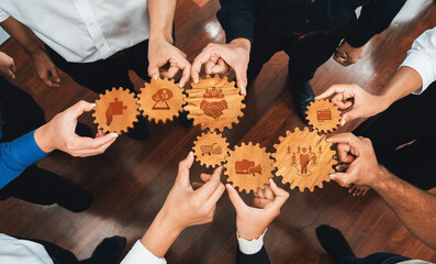 A diverse group of individuals collaborates around wooden gears with various icons, symbolizing...