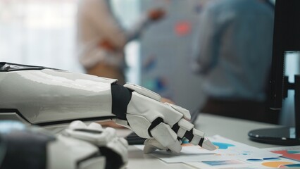 A close-up of a robotic hand interacting with business documents in an office, showcasing automation technology and collaborative work in a modern environment.Noogenesis