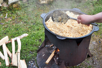Top view of the cooking process of pilaf over an open fire in a cauldron on a grill, with boiling...