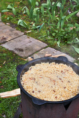 Top view of the cooking process of pilaf over an open fire in a cauldron on a grill, with boiling rice and rising steam, outdoors in summer.