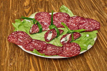 Slices of dry salami with cheese filling tied by green onion on lettuce leaves on a wooden table. Concept of festive appetizer presentation