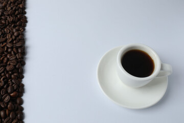 Hot coffee in a white coffee cup and many coffee beans scattered around 