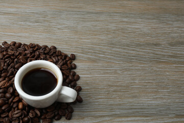 Hot coffee in a white coffee cup and many coffee beans scattered around 