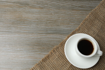 Hot coffee in a white coffee cup and many coffee beans scattered around 