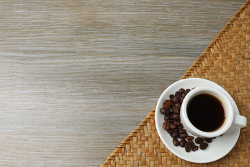 Hot coffee in a white coffee cup and many coffee beans scattered around 
