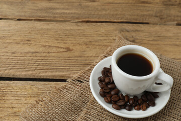Hot coffee in a white coffee cup and many coffee beans scattered around 
