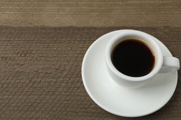 Hot coffee in a white coffee cup and many coffee beans scattered around 