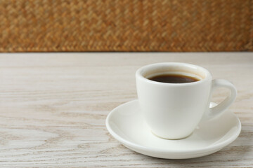 Hot coffee in a white coffee cup and many coffee beans scattered around 