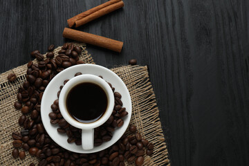Hot coffee in a white coffee cup and many coffee beans scattered around 