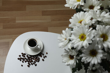 Hot coffee in a white coffee cup and many coffee beans scattered around 