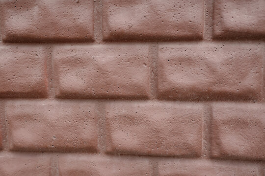 Close-up of a decorative pinkish-red brick wall with a porous textured surface. Ideal for backgrounds, construction materials, or architectural design elements.
