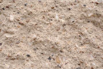 Close-up of a light beige concrete wall with rough texture and visible natural stone aggregate. Ideal for use as a background or construction material texture.