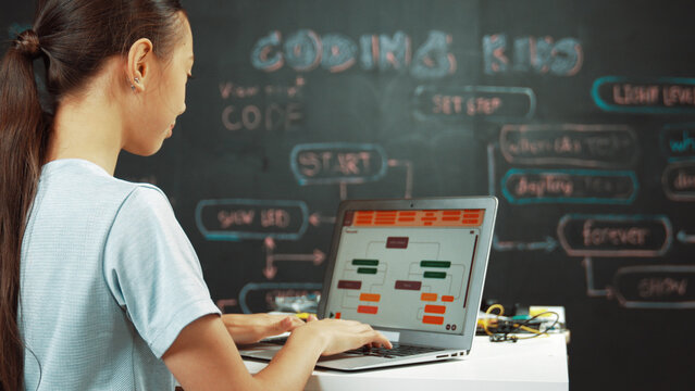 Smart girl programing system by using laptop at blackboard. Highschool student writing engineering code or prompt while looking at screen at STEM technology class. Creative education. Edification.