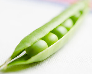 Close-up of fresh green peas inside an open pod on a light textured surface with soft natural lighting