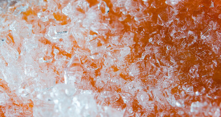 Macro shot of crushed ice crystals resting on a surface of bright orange papaya showing intricate texture and contrast