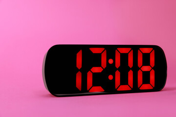 Digital alarm clock showing 12:08 o'clock on pink background, closeup
