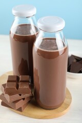 Tasty chocolate milk and pieces on white table against light blue background, closeup