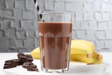 Tasty chocolate milk in glass, pieces and bananas on white table, closeup